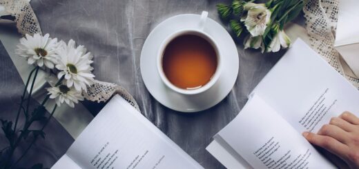 white ceramic teacup with saucer near two books above gray floral textile